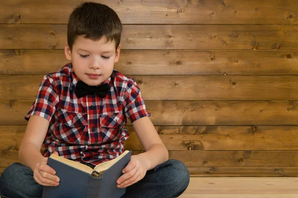 소년은 나무 벽 배경에 대 한 책을 읽고 하는 바닥에 앉아 — 스톡 사진
