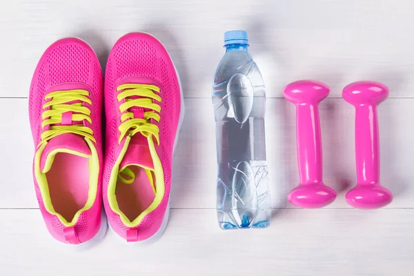 Conjunto feminino para praticar esportes, com halteres cor de rosa, em um piso de madeira leve e uma garrafa de água — Fotografia de Stock