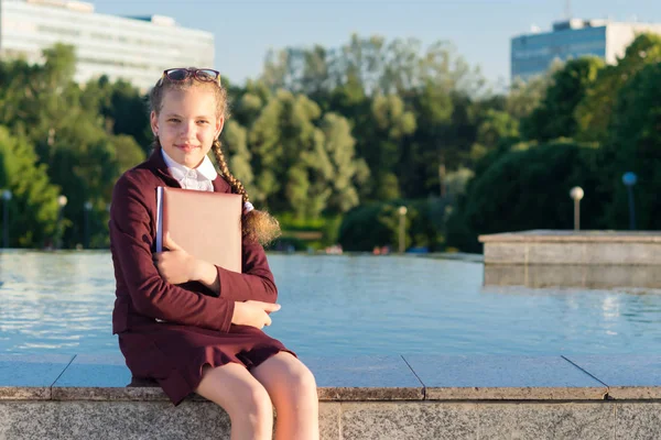 Flicka i skolan kläder sitter och håller en mapp — Stockfoto