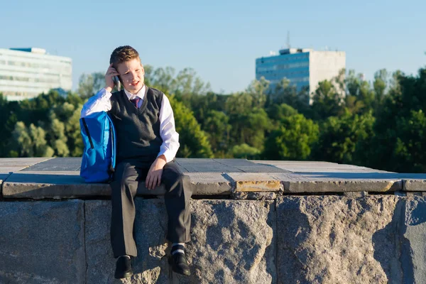 Skolpojke med en ryggsäck som sitter och pratar i telefon — Stockfoto