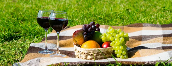 A basket of fruit and two glasses of wine on a green lawn for relaxing