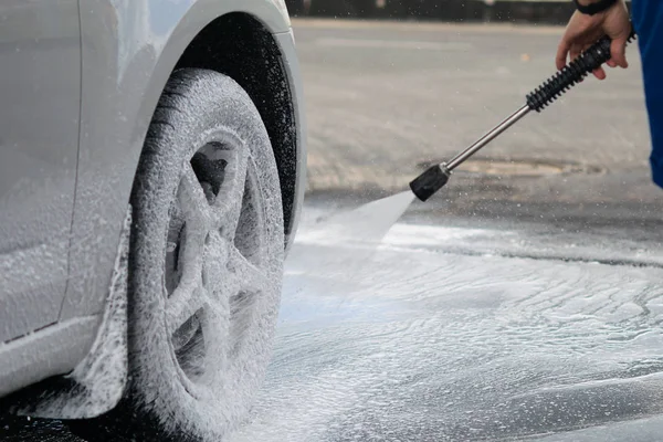 A strong water pressure washes off a thick foam from the wheels of the car — Stock Photo, Image