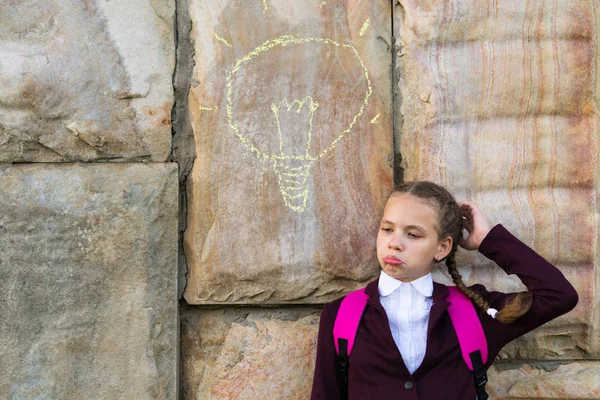 Девушка в школьной форме думает, лампочка нарисована на стене — стоковое фото