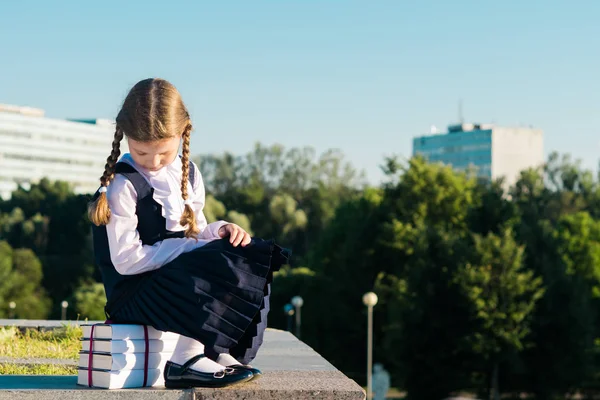 Liten skolflicka sitter på en lärobok för skolan — Stockfoto