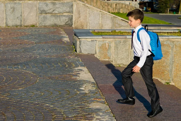 En pojke med en blå ryggsäck bakom honom, efter skolan, klättrar i trappan till toppen — Stockfoto