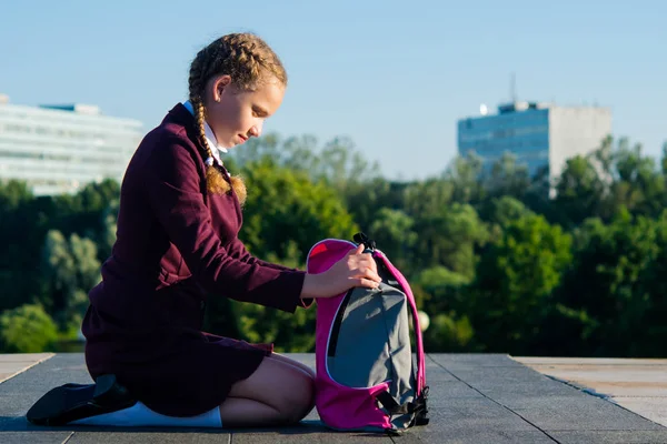 En flicka i de höga klasserna, tar ut läroböcker från en rosa ryggsäck i fria — Stockfoto