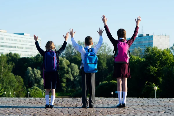 Three schoolchildren amicably walking in the park, and raise their hands upwards — Stock Photo, Image