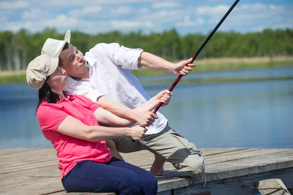 Hombre ayuda a una mujer a atrapar un pez de un muelle en el río —  Fotos de Stock