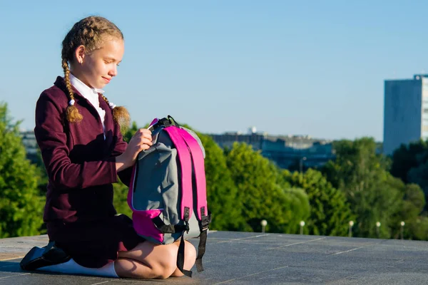 Het meisje zit op haar knieën en neemt de schoolboeken van haar rugzak — Stockfoto