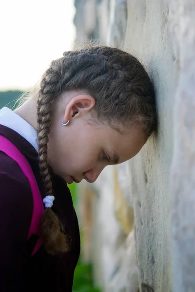 Flicka med flätor, sätta pannan mot stenmuren, efter skolan — Stockfoto