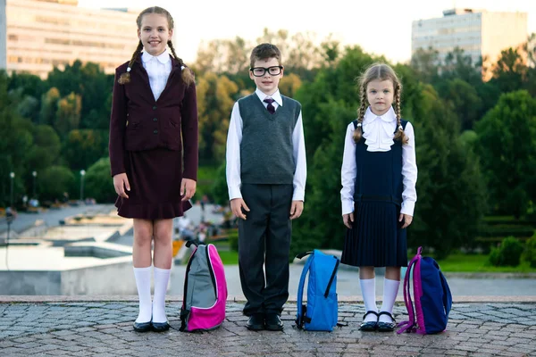 Tres escolares con carteras se paran en el crecimiento en la calle —  Fotos de Stock