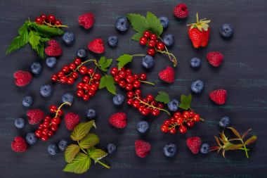 Kırmızı ve mavi çilek yeşil yaprakları ile bir dizi ile siyah arka plan