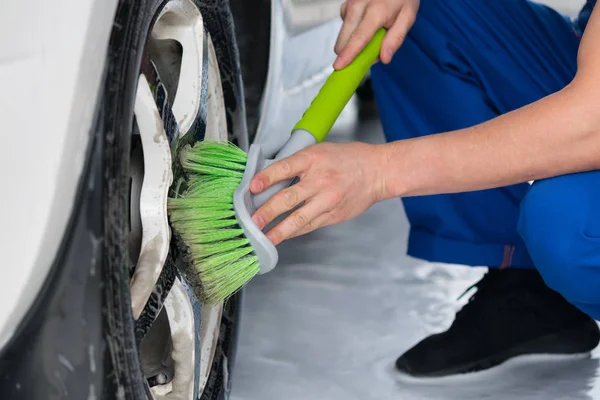 Trabajador lava la rueda del coche con un jabón verde cepillo — Foto de Stock