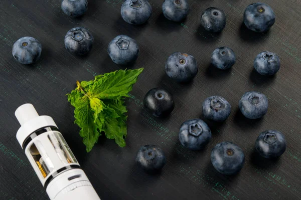 Vit elektronisk cigarett, på en svart målad bräda, bredvid blåbär och mynta — Stockfoto