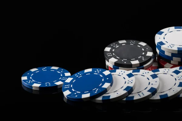 Kepingan poker dengan warna yang berbeda, tersebar panjang pada permukaan reflektif hitam — Stok Foto