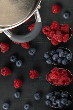 Berry Ahududu ve yaban mersini, yalan siyah bir zemin üzerine dört kaşık içinde köşede yemek bir gemi olduğunu