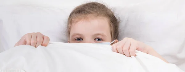 Маленькая девочка спряталась в постели в медицинской маске, чтобы защитить себя от инфекции. — стоковое фото