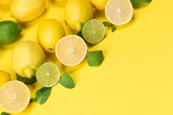 Limão e limão verde com fatias fatiadas e folhas de frutas cítricas encontram-se no canto do fundo amarelo — Fotografia de Stock