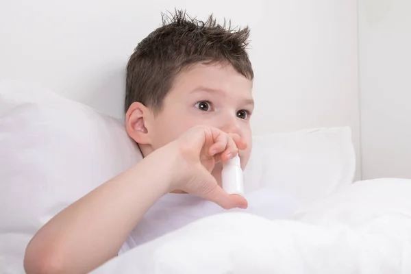 the boy is treated for a runny nose with a spray for the nose, right in bed