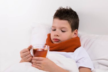 Çocuk yatakta bir boğaz hastalığı olan çay içer