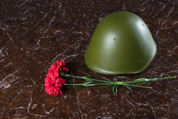 on a marble brown background is a military helmet and red flowers