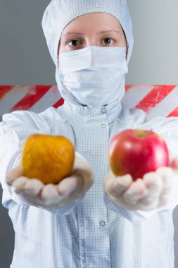 Beyaz koruyucu kıyafetli bilim adamı tutan 2 elma, taze ve enfekte