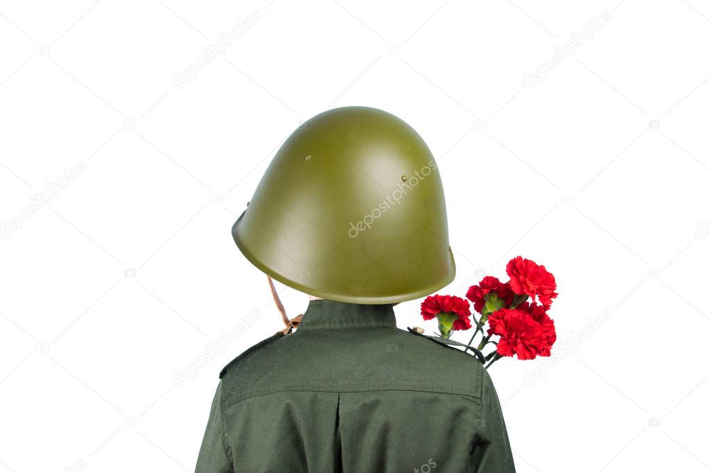 a child in military uniform and a helmet stands with his back, holding a carnation, in front of a white background