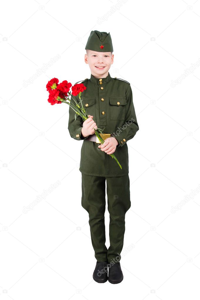 boy stands in military uniform and cap, with carnations in hands, on white background