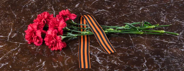 Red flowers and an orange ribbon lie on a marble slab