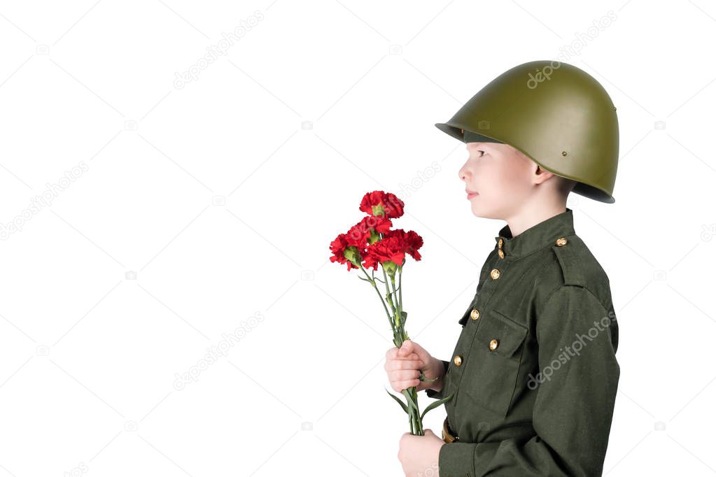 a boy in a helmet wearing a military uniform stands facing sideways and holding red flowers, isolated on white