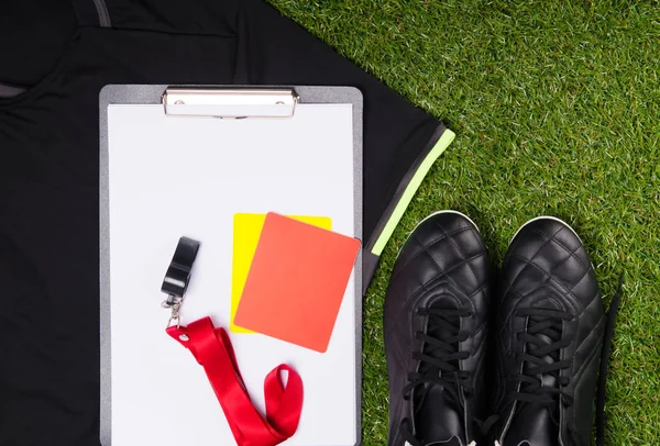 on the background of the grass, lies a sports T-shirt, boots, a recording tablet, a whistle and penalty cards for a judge, on a football match