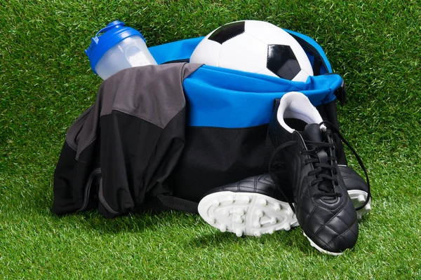 çizme, futbol topu, T-shirt ve çim çerçevede bir spor çanta içinde bir su şişesi