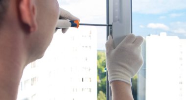 Eldiven ustası, tornavidayla plastik pencereyi tamir ediyor.