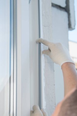 Eldivenli bir el işçisi, plastik pencere lastiğinin çerçevesine yapıştırır.