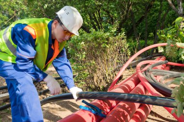 Tulumlu, beyaz kasklı ve gözlüklü bir adam borularla iş yapar.
