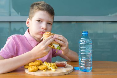Çocuk restoranda otururken tepsiden fast food yiyor.