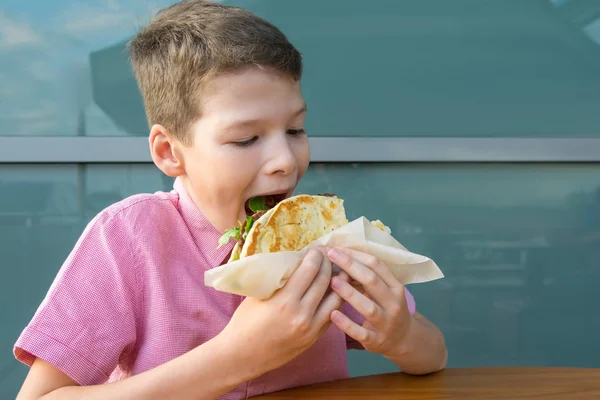 ファーストフード店のテーブルに座りながらサンドイッチを食べる少年 — ストック写真