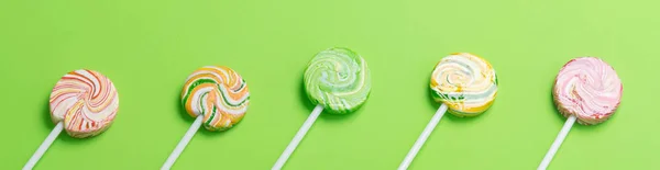 multi-colored caramel candies on a stick lie on a green background, long photo