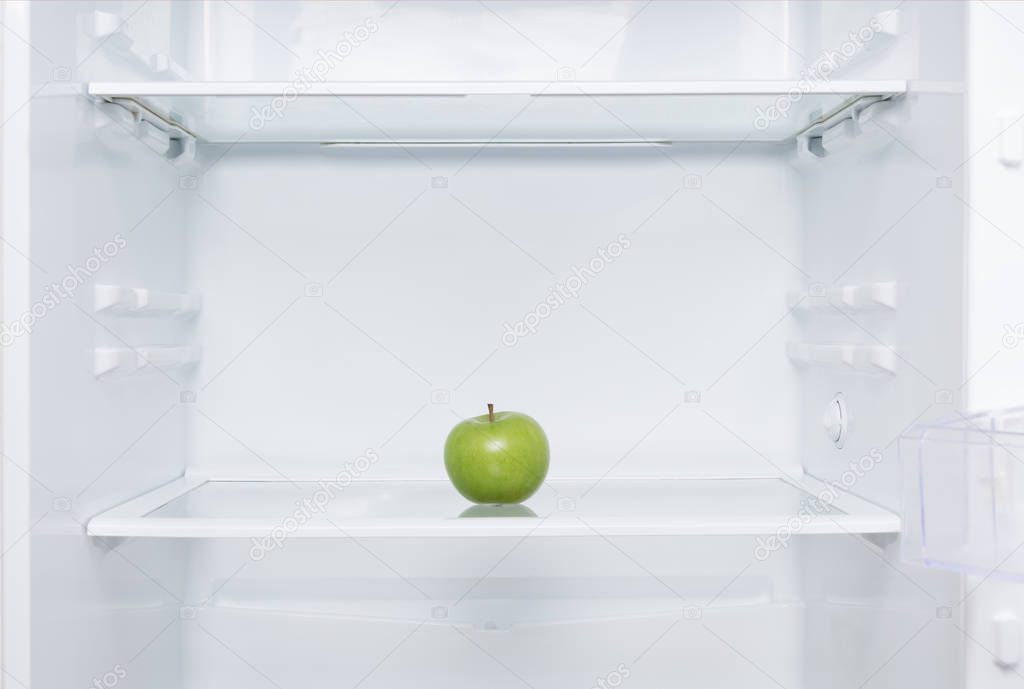 green fresh apple lies on a shelf in an open white refrigerator
