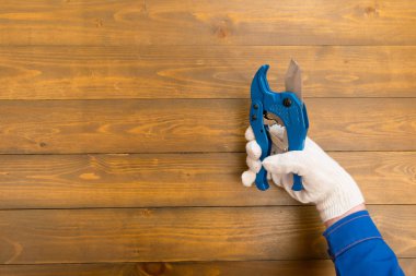 Koyu renk ahşap arka planda, beyaz eldivenli bir işçi, kesim malzemeleri için mavi makas tutuyor, bir yer var.