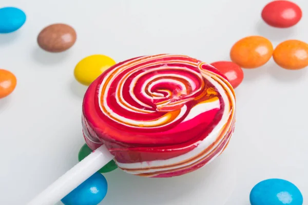 close-up of a red Lollipop on a stick, on a white table and colorful dragees
