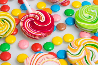 Beyaz bir masada, yakın plan, renkli lolipoplar ve jelibonlar serilmiş.