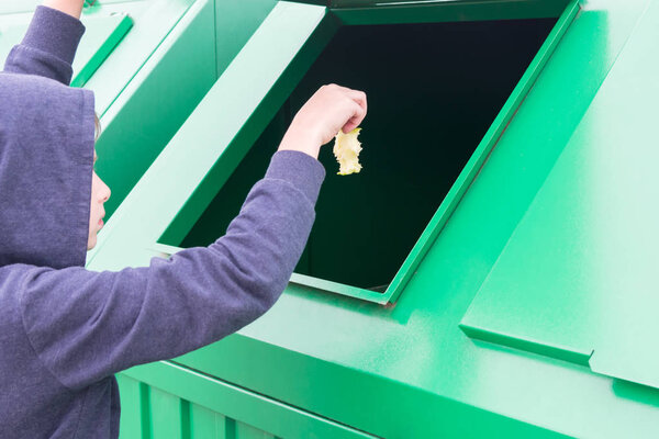 Человек бросает корешок с съеденного яблока в мусорный бак
