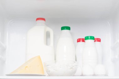 Buzdolabının üst rafında beyaz şişeler ve bir parça peynir var.