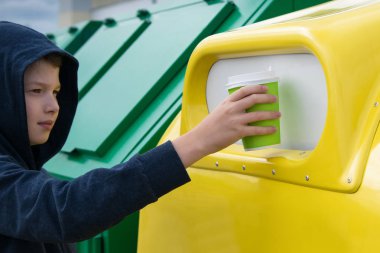 Çocuk geri dönüşümler için özel bir kabın içine atmak üzere bir kağıt bardak getirdi.