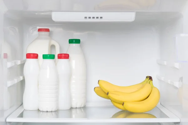 yogurts and bottled milk on a shelf in the refrigerator with bananas, light breakfast