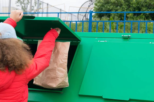 girl in a red jacket, throws a paper bag in a dumpster, rear view