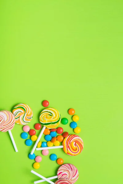 colorful lollipops on a stick and jelly beans, on a light green table, there is a place for the inscription