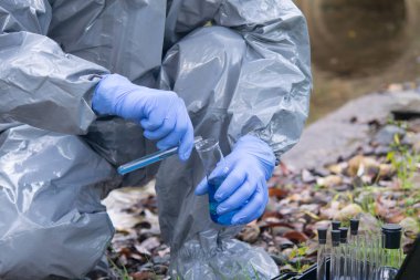 Mavi eldivenli koruyucu kıyafetli bilim adamı deney tüpünden mavi bir sıvıyı şişeye boşaltıyor.