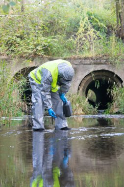 Koruyucu giysi ve maske uzmanı cihazı ölçüp göletin üzerinde elinde tutuyor.